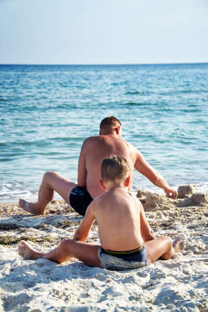father and his son playing together in sand on beachの写真素材