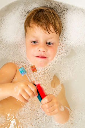 The little boy bathes in a bathroom and brush his teeth.