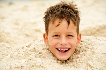 little boy buried in the sand on beachの写真素材