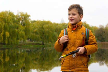 Side view on boy in yellow jacket using fishing rod outdoors at pond during cool autumn dayの写真素材
