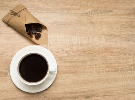 Cup of coffee, pieces of chocolate with hazelnut in paper package on wooden background. Top viewの写真素材