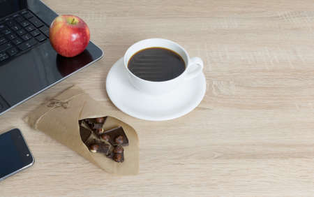 Top view of working place elements,Working wooden table with empty space, laptop, apple, coffee cup, dark chocolate with hazelnutの写真素材