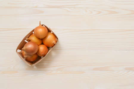 Onions in a wooden box on white wooden table. Top view. Space for textの写真素材