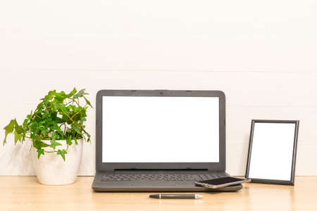 Laptop mock up on wooden table with photo frame, ivy plant in pot. Working space in loft. Interior...