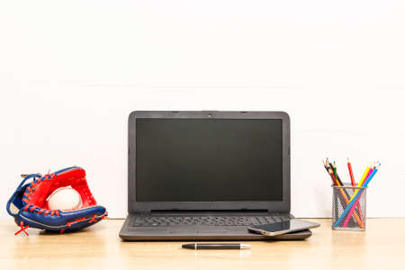 Laptop on wooden table with baseball glove and ball, pen, colored pencils and smart phone Working...