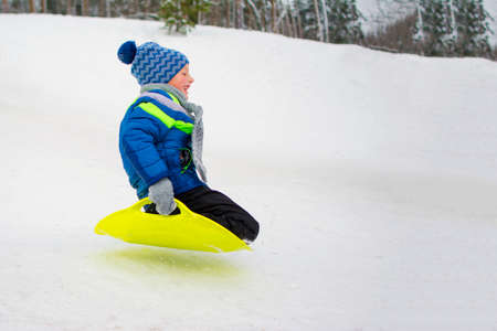 Kid flies down a hill on plate for driving on snowの写真素材