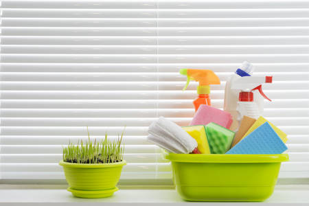 Cleaning supplies and green grass in the pot against window blindesの写真素材