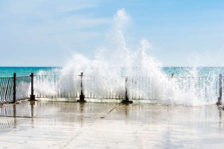 Big waves crushing on curved stone pier, on sunnny weather, big tide.