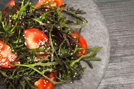 Fresh salad; juicy tomatoes, fresh arugula, ,olive oil and sesame seeds on black stone background....