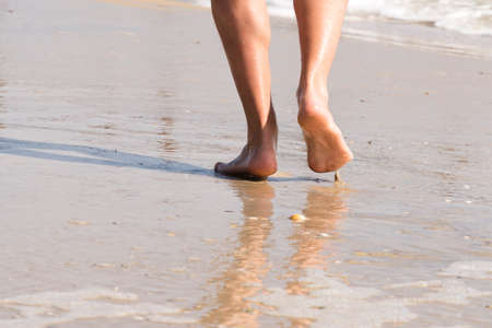 Walking barefoot along the surf on the sand beach at sunset; close upの写真素材