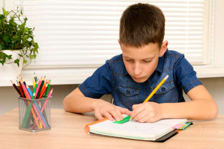 Boy draw in notebook. Child sitting at the desk home and doing his homework. School, children,...