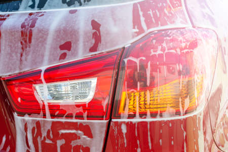 Car wash background. Close up of rear taillight on black modern luxury car covered with washing foam-soapの写真素材