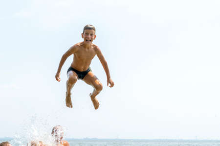 Happy ten years boy jumping in to water on wide river from the air. Summer vacation fun conceptの写真素材