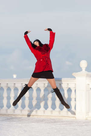 Beautiful young woman at winter. Attractive brunette in red jumping in the winter parkの写真素材