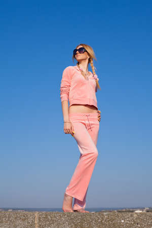 Attractive young woman in pink sportswear posing on background of sky  Girl in sunglasses on open airの写真素材