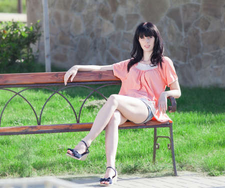 Brunette in shorts on open air. Attractive young woman in shorts sitting in garden on benchの写真素材