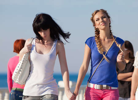 Girls on quay. Two attractive young women walking along seafrontの写真素材