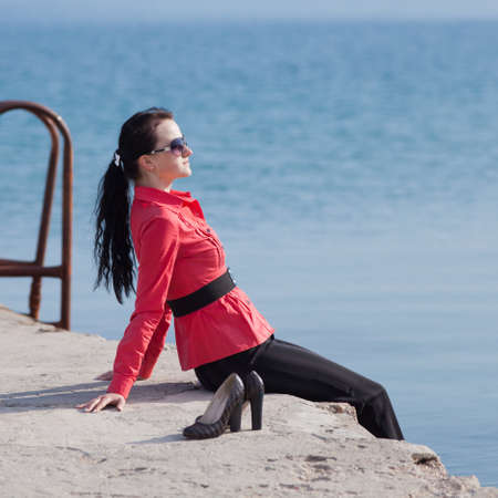 Young woman on seashore  Brunette in a red blouse sitting on the pier at the seaの写真素材