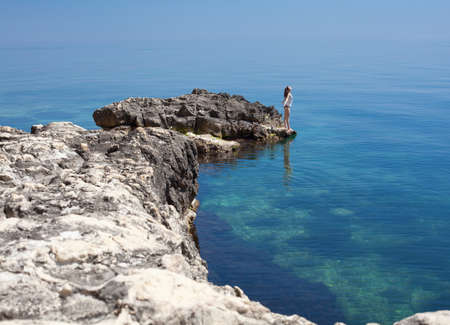 Seascape with young woman on rocky shore  Brunette on rock at the seaの写真素材