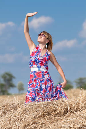 Country girl on a hayloft with arm raised  Young woman posing on haystack looking up smilingの写真素材