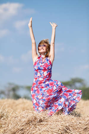Country girl on a hayloft  Young woman in sunglasses with hands raised standing on hayloftの写真素材