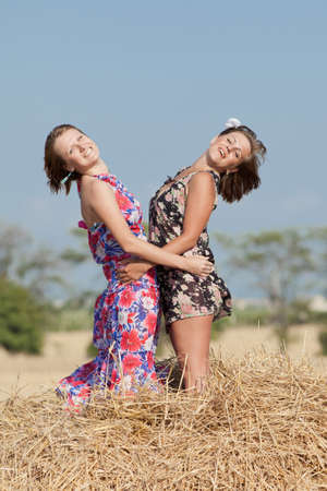 Two girls in field  Two young woman posing on hay looking at camera smilingの写真素材