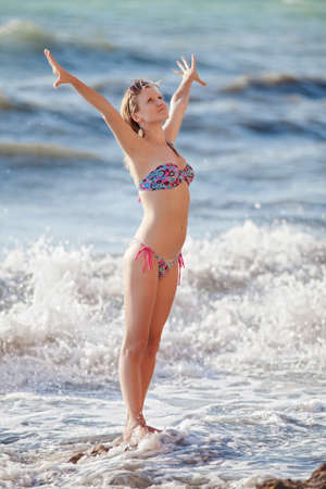 Girl at the sea  Attractive young woman with hands raised standing in line of surfの写真素材