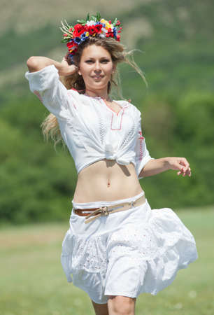 Ukrainian girl in field  Attractive blond woman in ukrainian wreath and blouse with ukrainian embroidery running along field  Vertical compositionの写真素材
