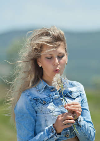 Portrait of blond girl outdoors  Attractive young woman blowing on fetus of wild flower like a dandelionの写真素材