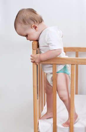 Charming child in the crib   Charming baby stands in child bed and looking downの写真素材