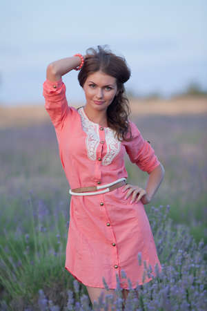 Young woman in the field of blossoming lavender. Portrait of attractive girl in pink dress in field of blooming lavenderの写真素材