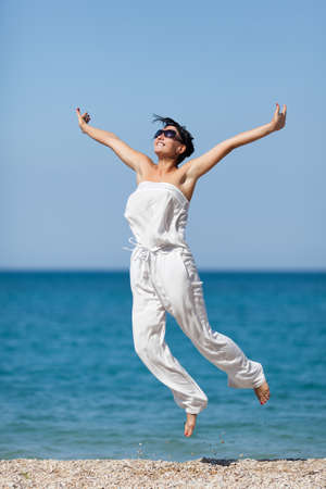Girl at the sea  Young woman in jumpsuit jumps on seashoreの写真素材