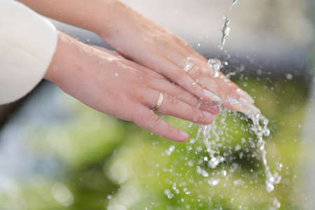 Hands of newly wedded with wedding rings on their fingers under running waterの写真素材