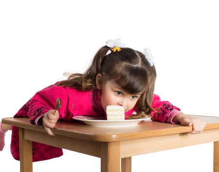 Charming preschooler in pink lays on table and eats cake. Little girl eating dessertの写真素材