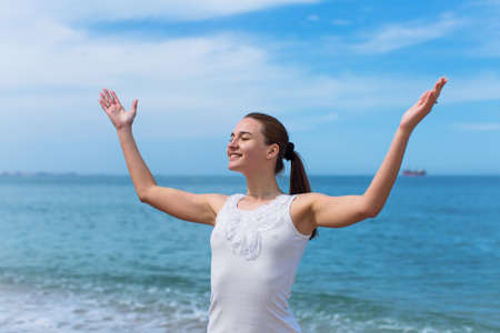 Girl at the sea. Young woman with arms raised and eyes closed against the sea