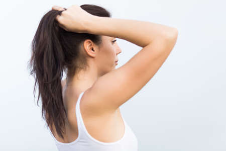 Girl on open air. Attractive young woman in white tank top adjusts her hairstyle rear viewの写真素材