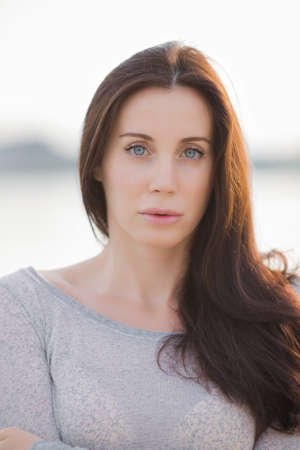 Longhaired brunette on open air. Portrait of attractive young woman in gray sportswear looking at cameraの写真素材