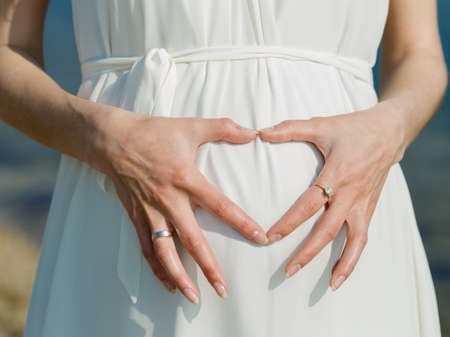 Woman posing heart on her belly. Expectant mother posing a heart with fingers on her belly