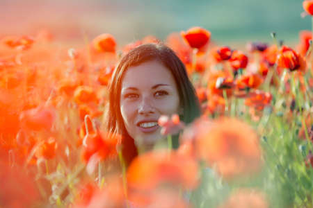 Girl at blooming poppy field. Portrait of young women in poppiesの写真素材