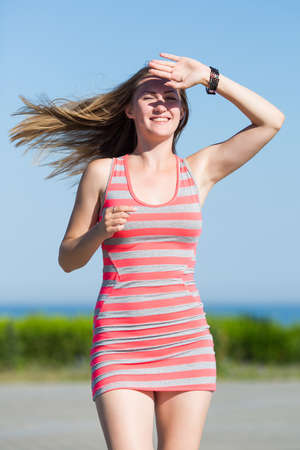 Portrait of girl in striped dress on open air. Long haired blonde runs hiding her eyes from sunの写真素材