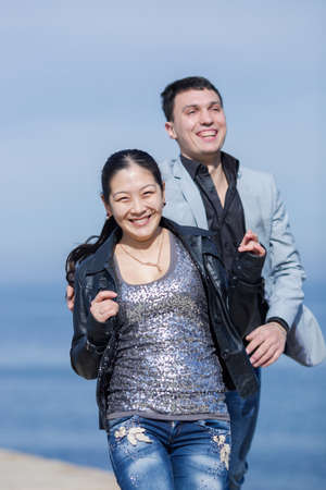 Attractive couple running along of pier. European guy catches his asian girlfriend