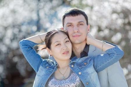 Portrait of attractive couple in blossoming park. Asian girl and european guy posing against of blossoming almond treesの写真素材