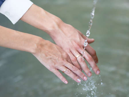 Wedding hands. Hands of newly wedded with wedding rings on their fingers under running waterの写真素材