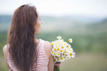 Girl with chamomile. Young woman in pink sleeveless dress with bouquet of chamomile, rear viewの写真素材