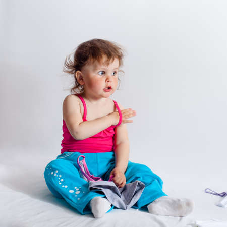 Baby playing in studio on white background. Charming baby in blue trousers and red tank top playing with baby clothesの写真素材