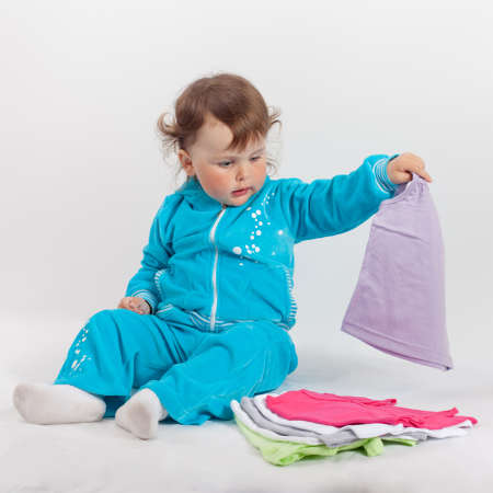 Baby playing in studio on white background. Charming baby in blue rompers playing with baby clothesの写真素材