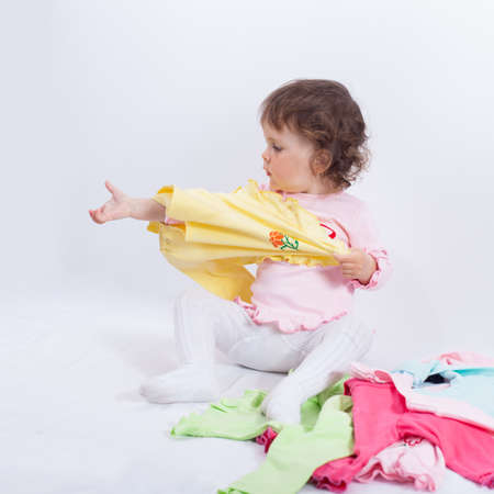 Child puts yellow blouse on. Charming baby playing with clothes in studio on white backgroundの写真素材
