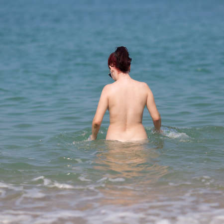 Skinny-Dipping. Not tanned naked young woman enters in sea, rear view, square compositionの写真素材