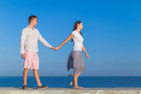 Attractive couple on seafront. Young man and young woman walking along concrete pier