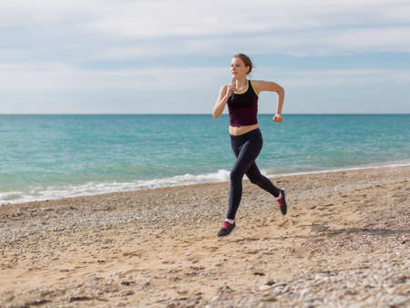 Jogging. Young sportswoman running along the beach in evening timeの写真素材